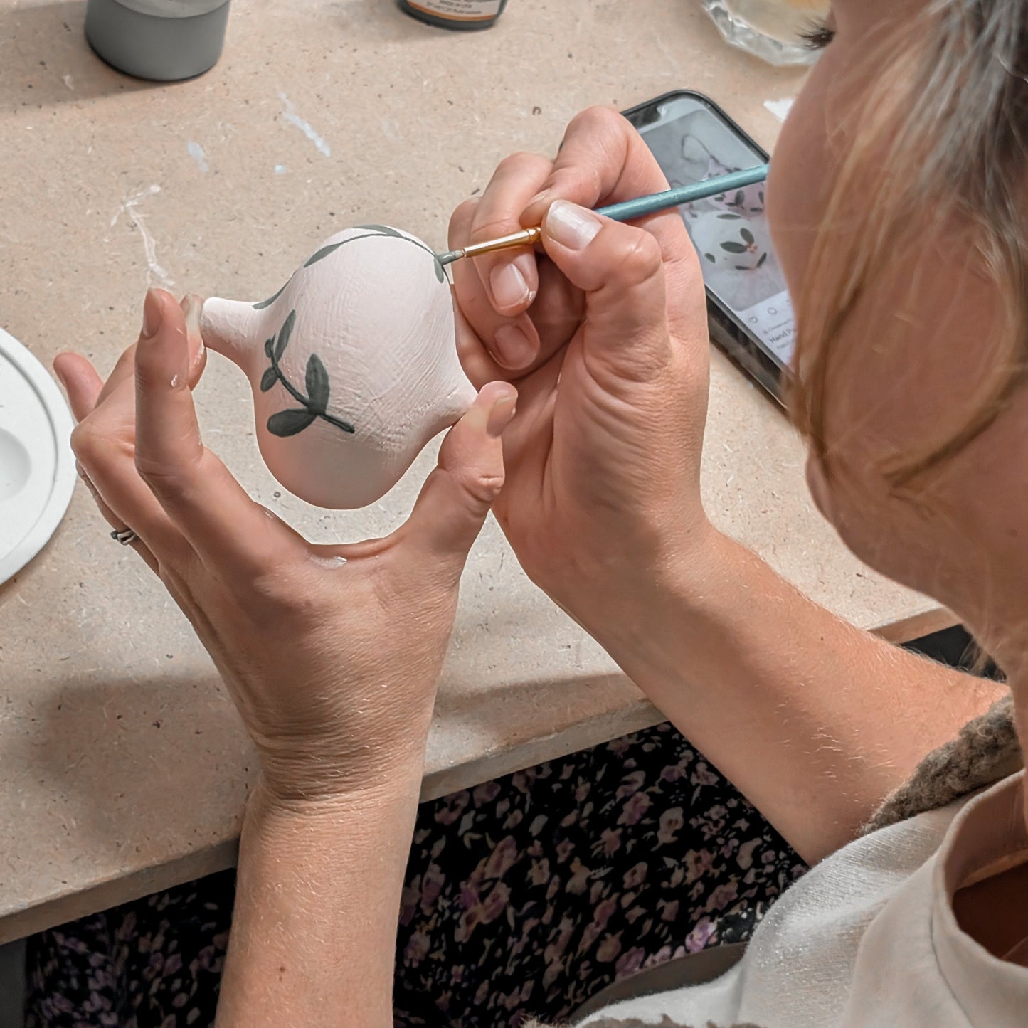 Person painting a small ceramic object with a brush on a table.
